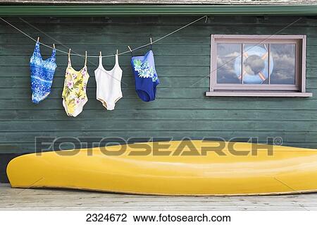 Stock Image - Bathing Suits On Clothes Line With Yellow Canoe Against Cottage, Ontario, Canada. Fotosearch