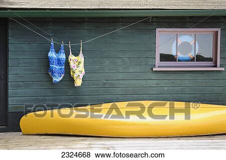 Stock Photo - Bathing Suits On Clothes Line With Yellow Canoe Against Cottage, Ontario, Canada. Fotosearch