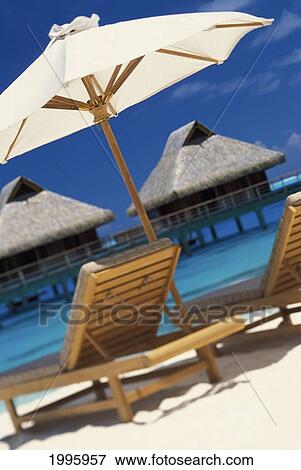 Stock Photo - Beach Chairs And Umbrella On Beach With Tranquil Ocean And Thatched Bungalows. Fotosearch