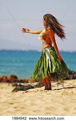Stock Image - Beautiful Hawaiian girl dancing hula on ocean shoreline. Fotosearch