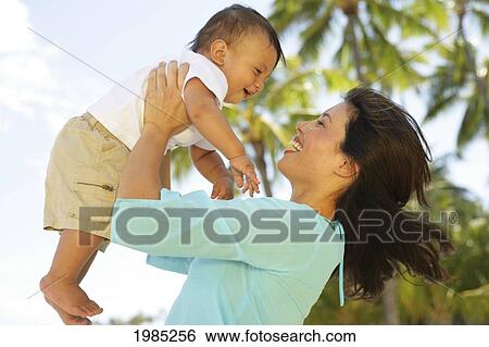 Beautiful Local Mother Holding Little Boy Up In The Air At The Beach, Palm Tree In Background. View Large Photo Image Stock Photograph - Beautiful Local Mother Holding Little Boy Up In The Air At The Beach, Palm Tree In Background.. Fotosearch