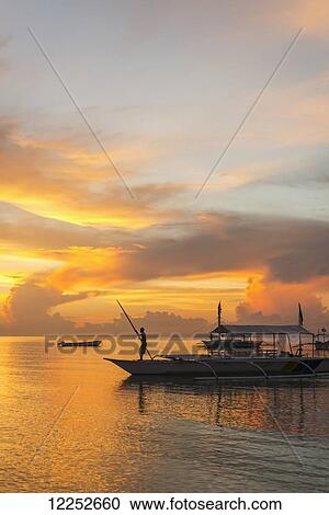Beautiful sunrise in Alona Beach, a man moving his boat to reach the shore with a long stick; Panglao Island, Bohol, Philippines View Large Photo Image Stock Image - Beautiful sunrise in Alona Beach, a man moving his boat to reach the shore with a long stick; Panglao Island, Bohol, Philippines. Fotosearch