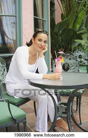 Beautiful Young Woman Sits At An Outdoor Table With A Tropical Cocktail View Large Photo Image Stock Photograph - Beautiful Young Woman Sits At An Outdoor Table With A Tropical Cocktail. Fotosearch