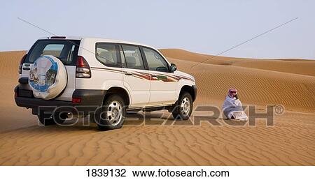 Stock Image - Bedu Guide Waiting By Car; Wahiba, Oman. Fotosearch