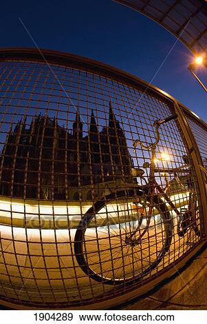Stock Photo - Bicycle Against Wire Fence At Dusk, Cologne Cathedral (Kolner Dom) In Background, Cologne, Germany. Fotosearch