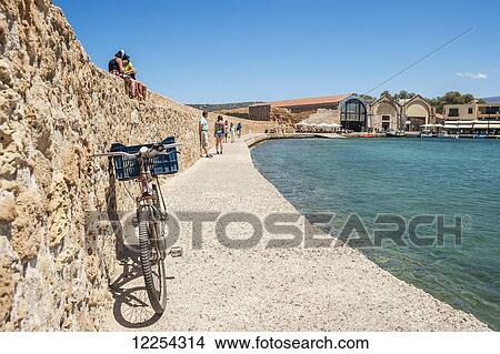 Picture - Bicycle and pedestrians on the wall along the Venetian harbour; Chania, Crete, Greece. Fotosearch