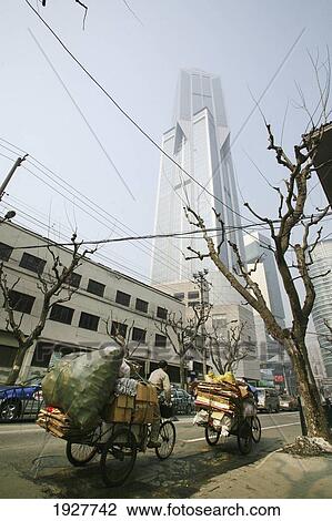 Stock Image - Bicycle Rickshaw Carrying Rubbish Past Modern Skyscrapers, Shanghai, China. Fotosearch