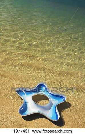Stock Image - Blue And White Star Swim Ring Resting At On The Beach.. Fotosearch