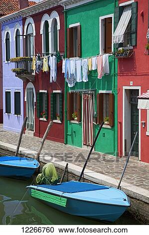 Stock Image - Blue boats sit in front of a row of colourful houses; Burano, Venice, Italy. Fotosearch