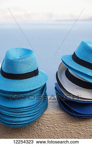 Stock Image - Blue hats in a pile on a wall with a view of the water; Oia, Santorini, Greece. Fotosearch