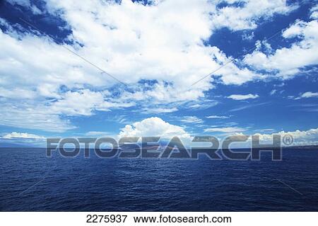 Stock Photo - Blue sky and cloud with the coastline of an hawaiian island in the distance; Hawaii, United States of America. Fotosearch