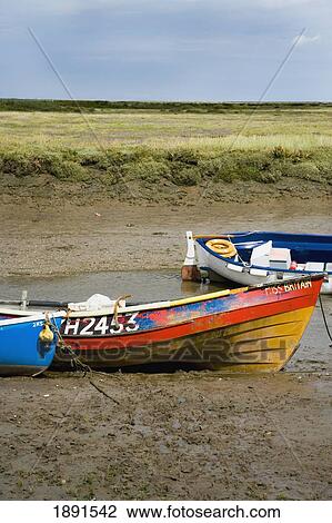 Stock Image - Boats In Mud Of Small Estuary By Marshes. Fotosearch