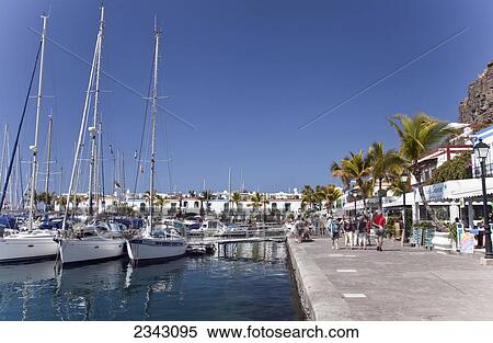 Boats In The Harbour And Pedestrians On The Promenade; Puerto Morgan, Gran Canaria, Spain View Large Photo Image Stock Photography - Boats In The Harbour And Pedestrians On The Promenade; Puerto Morgan, Gran Canaria, Spain. Fotosearch