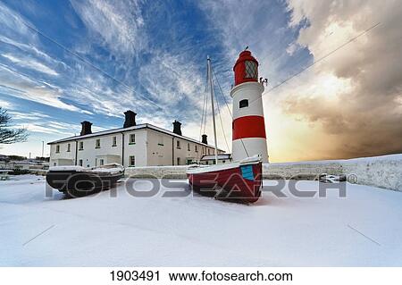 Stock Image - Boats Sitting On A Frozen Surface With A Lighthouse And Building In The Background; South Shields, Tyne And Wear, England. Fotosearch