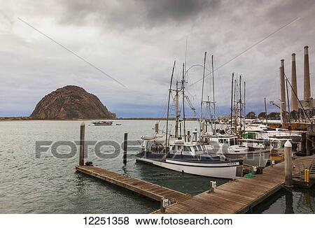 Stock Photo - Boats tied up to the dock in Morro Bay, with Morro Rock in the background; California, United States of America. Fotosearch