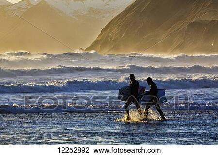 Stock Image - Body surfers walk in the water on the coast of Kodiak Island during late afternoon, Pasagshak State Park, Kodiak Island, Alaska. Fotosearch