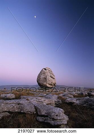 Stock Photo - Boulder On Limestone Pavement At Dusk, With Moon And Ingleborough Hill Behind, Twisleton Scars Near Ingleton, Yorkshire Dales National Park, North Yorkshire, England.. Fotosearch