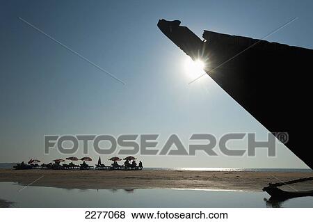 Stock Photo - Bow of old boat on beach with people sunbathing in background; Goa, India. Fotosearch