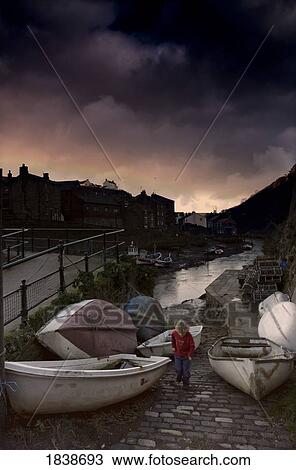 Stock Image - Boy Amongst Boats In Harbor Area; Staithes, Yorkshire, England, Uk. Fotosearch