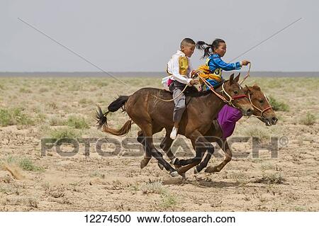 Stock Image - Boy and girl riding horses in the Daaga (two-year old) horse race held during the Naadam Festival in Mandal Ovoo,? mnÃƒÆ’Ã‚Â·govi Province, Mongolia. Fotosearch