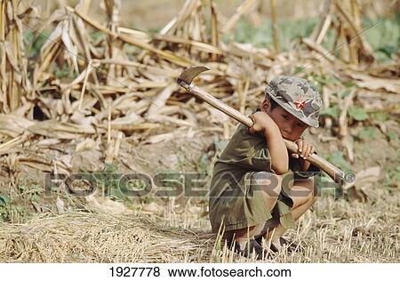 Stock Photo - Boy Crouching In Field With Tool. Fotosearch