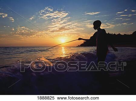 Stock Photography - Boy Fishing At Dusk On Beach Next To Kaya Mawa. Fotosearch