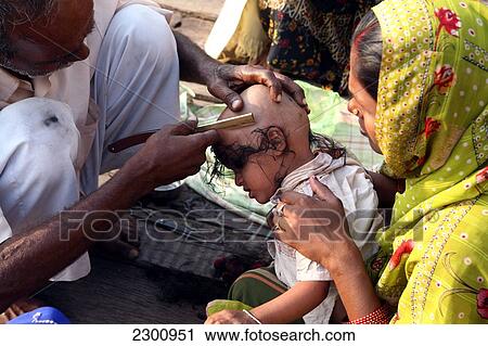 Stock Image - Boy having head shaved by street barber on bathing ghat above the River Ganges. Hindu tradition to have head shaved at auspicious times. The culture of Varanasi is closely associated with the River Ganges and the river's religious importance. It is the r. Fotosearch