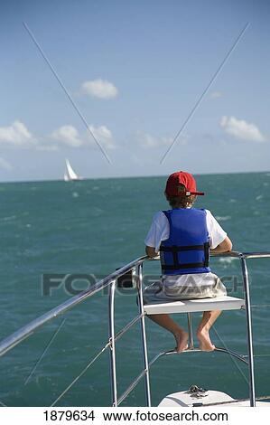 Picture - Boy In Life Vest Sitting On Edge Of Sailboat. Fotosearch