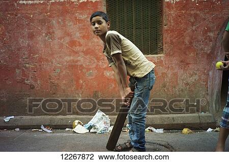 Stock Image - Boy playing cricket in an alley; Kolkata, West Bengal, India. Fotosearch