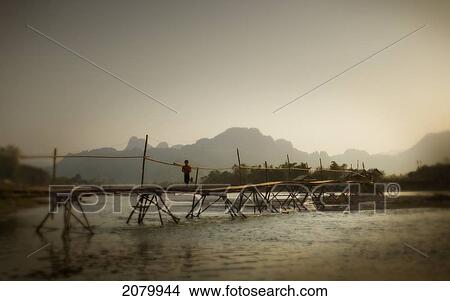 Boy Running Across A Wooden Bridge On A River With Mountains In The Background; Vang Vieng Laos View Large Photo Image Picture - Boy Running Across A Wooden Bridge On A River With Mountains In The Background; Vang Vieng Laos. Fotosearch