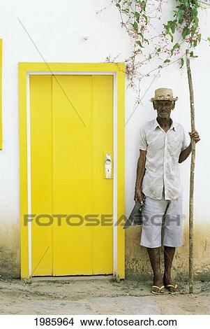 Picture - Brazil, Buzios, Local Man Standing Next To Yellow Door On Roadside.. Fotosearch