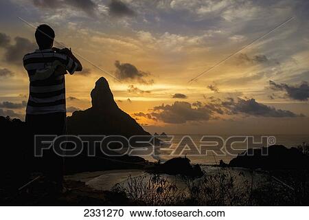 Brazil, Pernambuco, Man taking photograph of Morro do Pico at sunset from Forte dos Remedios; Fernando de Noronha View Large Photo Image Stock Image - Brazil, Pernambuco, Man taking photograph of Morro do Pico at sunset from Forte dos Remedios; Fernando de Noronha. Fotosearch