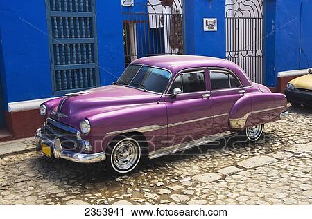 Stock Image - Bright Purple Chevy Parked In Front Of A Blue Building; Trinadad, Sancti Spiritus, Cuba. Fotosearch