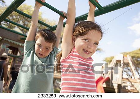 Stock Photo - Brother and sister play on monkeybars at playground; Oahu, Hawaii, United States of America. Fotosearch