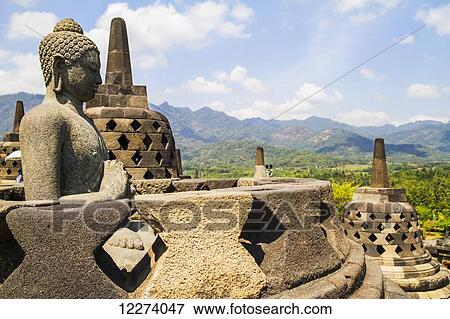Stock Photo - Buddha statue amidst the latticed stone stupas containing Buddha statues on the upper terrace, Borobudur Temple Compounds, Central Java, Indonesia. Fotosearch