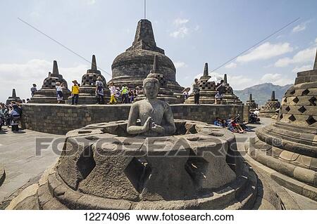Stock Photograph - Buddha statue amidst the latticed stone stupas containing Buddha statues on the upper terrace, Borobudur Temple Compounds, Central Java, Indonesia. Fotosearch