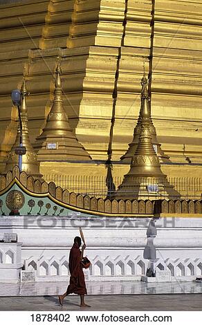 Stock Image - Buddhist Monk Passing By Historic Pagoda. Fotosearch