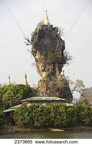 Stock Photography - Buddhist monks walk past Kyauk Kalap Pagoda and rock pillar; Kayin State, Burma. Fotosearch