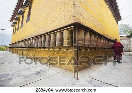 Picture - Buddhist temple wall with prayer wheels and a praying monk at Longwu Tibetan monastery; Tibet, China. Fotosearch