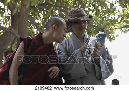 Stock Image - Buddhist Tourists Consulting Guidebook In Connaught Place, A Central Business District Of New Delhi, Uttar Pradesh, India. Fotosearch