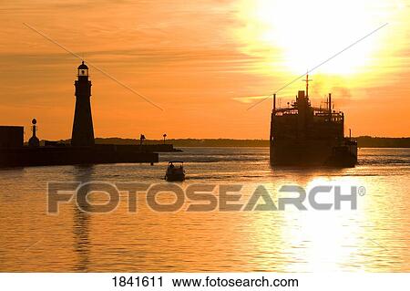 Stock Image - Buffalo Lighthouse And Cement Carrier In Buffalo Port At Sunset; Buffalo, New York State, Usa. Fotosearch