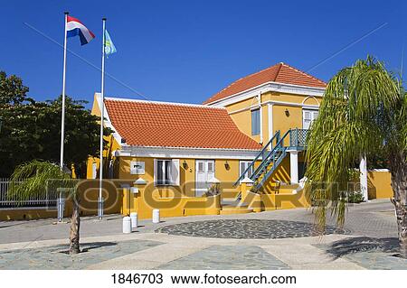 Building Exterior With Flags Weaving Outside; Monuments Office Of Aruba, Oranjestad, Aruba Island, Kingdom Of The Netherlands View Large Photo Image Stock Image - Building Exterior With Flags Weaving Outside; Monuments Office Of Aruba, Oranjestad, Aruba Island, Kingdom Of The Netherlands. Fotosearch