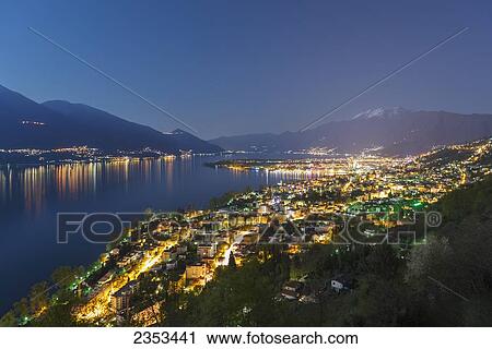 Stock Image - Buildings Along Lake Maggiore And The Swiss Alps Illuminated By Moonlight At Night; Locarno, Ticino, Switzerland. Fotosearch