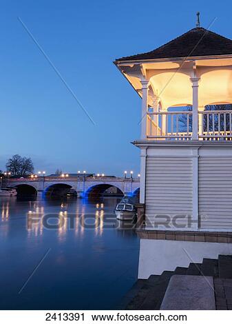 Stock Image - Buildings and a bridge along the river at dusk; Kingston Upon Thames, England. Fotosearch