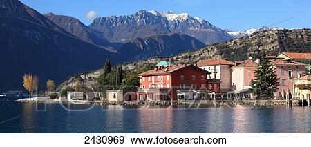 Stock Photo - Buildings and a view of the mountains along the shoreline of Lake Garda; Torbole, Trentino, Italy. Fotosearch