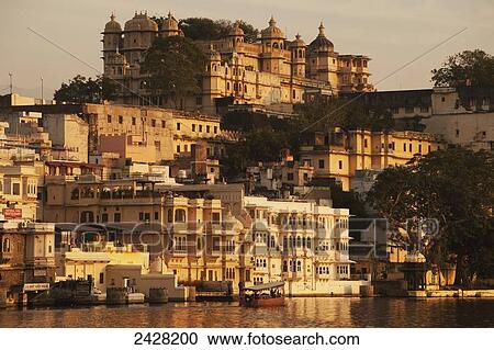 Stock Image - Buildings glowing in the sunlight of the setting sun along the river; Udaipur, India. Fotosearch
