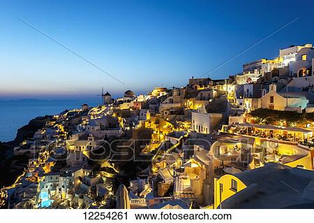 Stock Image - Buildings on a hillside illuminated at dusk; Oia, Santorini, Greece. Fotosearch
