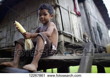 Stock Image - Bunong boy sitting on steps holding corn; Mondulkiri, Cambodia. Fotosearch