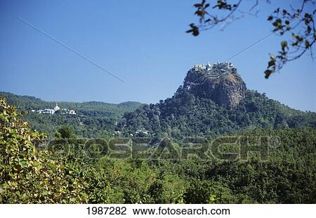 Stock Image - Burma (Myanmar), Bagan, Mount Popa, Temples On Hillside, Greenery In Foreground.. Fotosearch