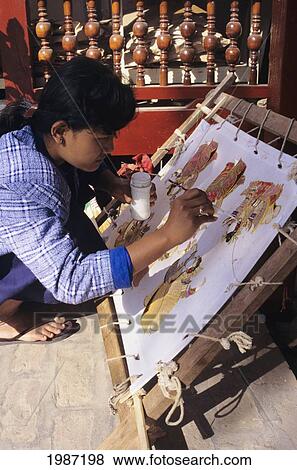 Stock Photo - Burma (Myanmar), Mandalay, Local Woman Handpainting Kalaga Tapestry In Shop, View From Side.. Fotosearch